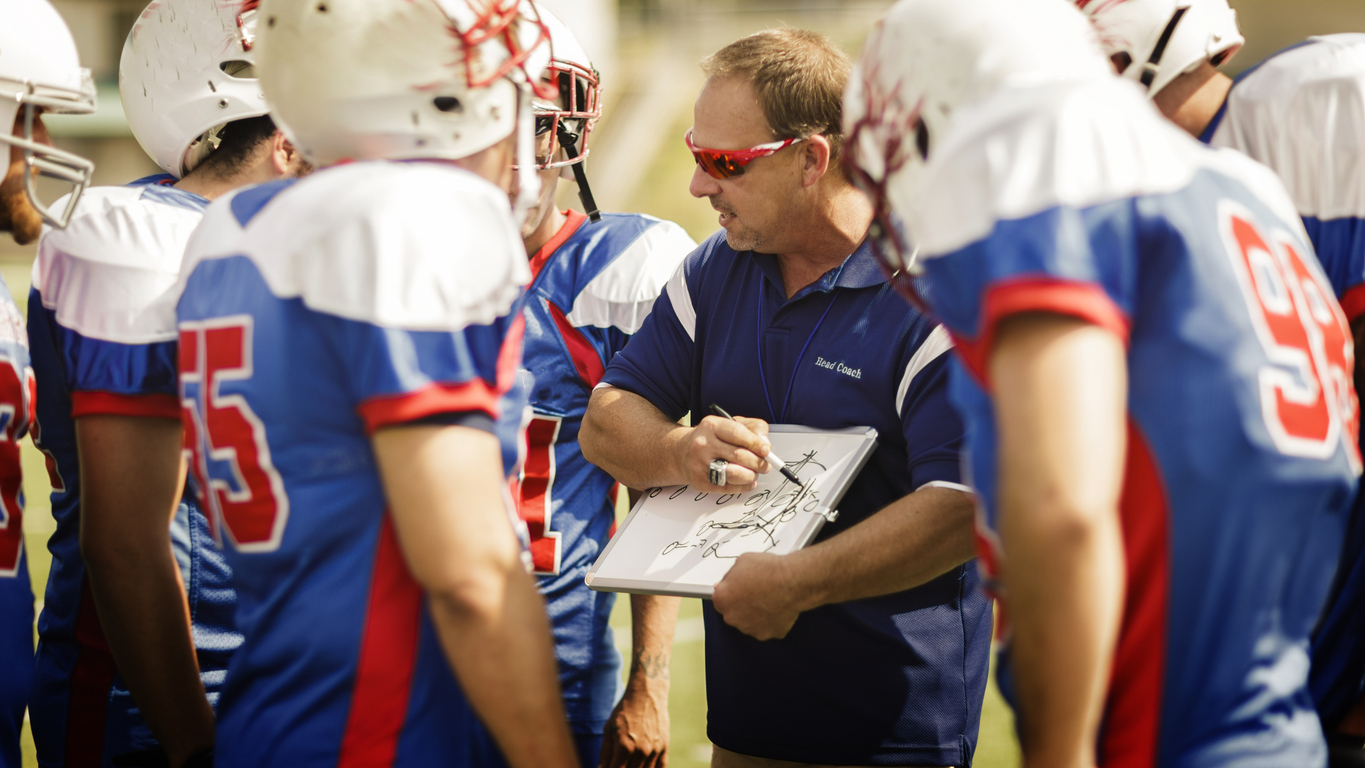 Close-up of a football coach holding a play call sheet on the field