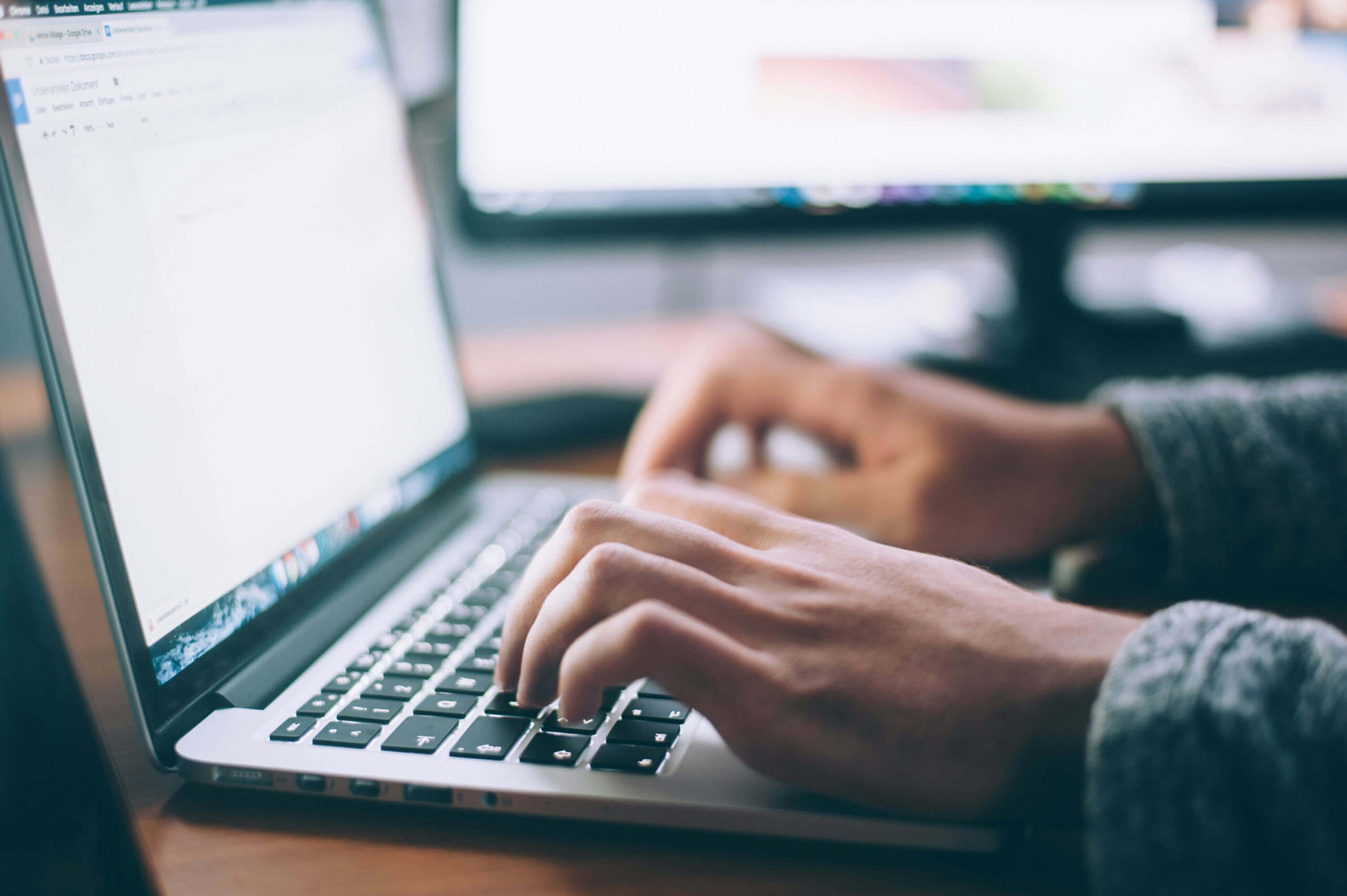 Hands typing on a laptop keyboard with a blurred screen showing a document