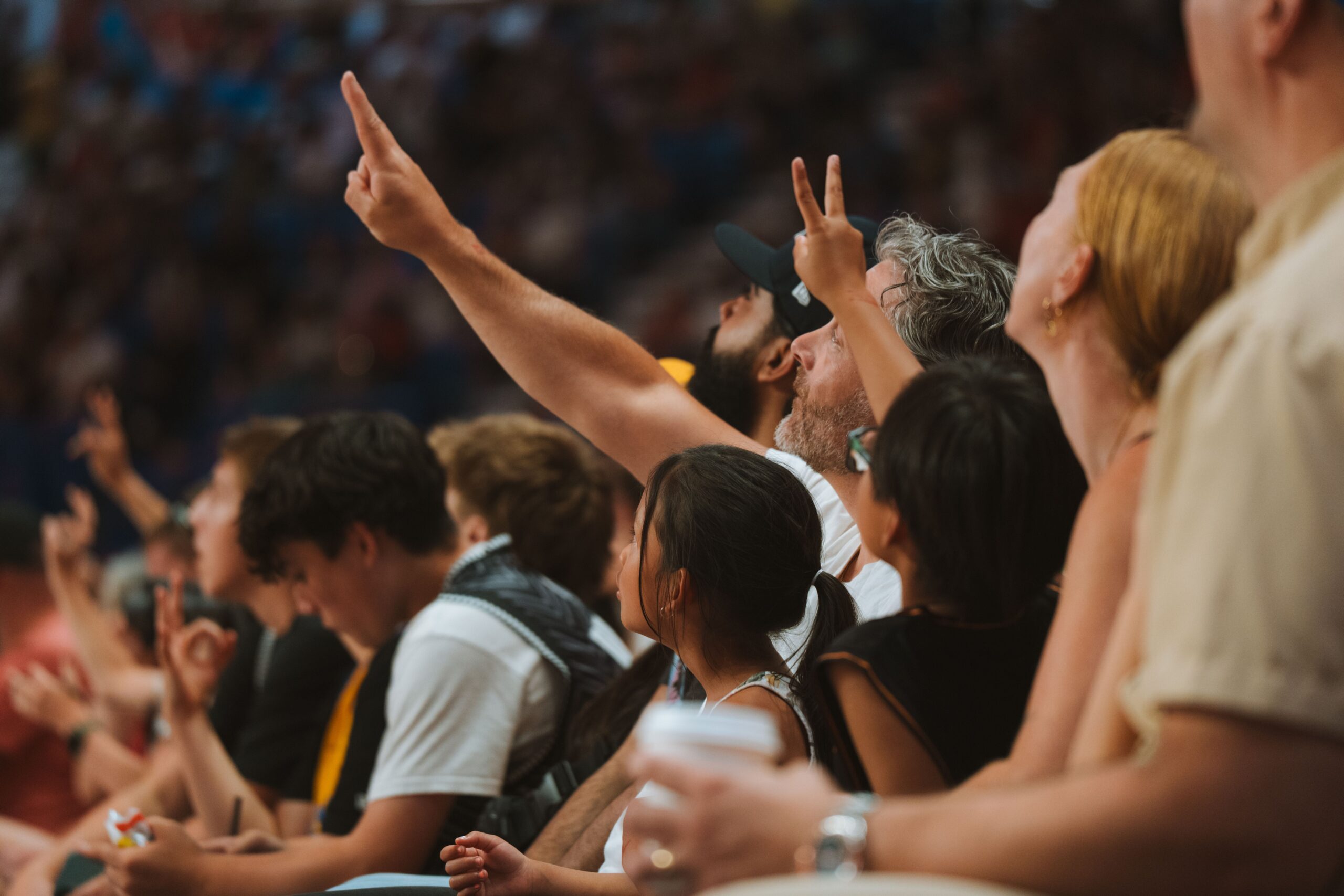Spectators in a crowd, some raising their hands, watching an event.