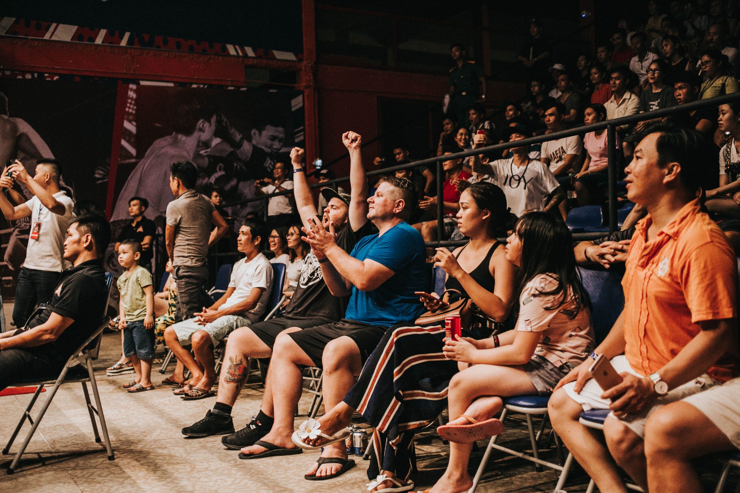 Spectators in a stadium, some cheering with fists raised, others watching intently.
