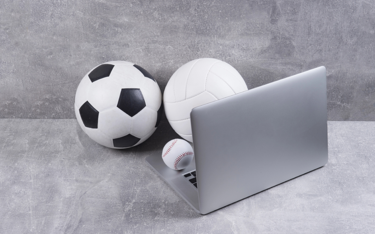 Soccer ball, volleyball, baseball, and laptop on a gray concrete surface