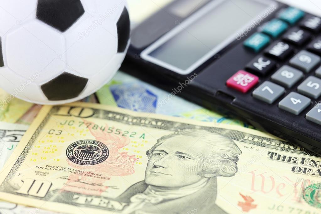 A soccer ball resting on a pile of one hundred dollar bills